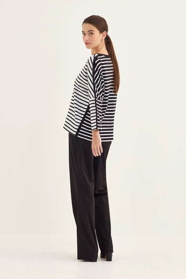 A woman modeling a black and white horizontally striped long-sleeve top with black wide-leg trousers by Verge, shown from a side-back angle against a plain white studio background.