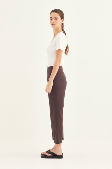 A woman shown in profile wearing a fitted white short-sleeve top, dark navy cropped pants by Verge, and black sandals against a plain light gray studio background.