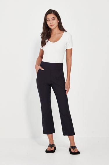 A woman modeling a white short-sleeve scoop-neck top and black cropped wide-leg pants by Verge with black sandals, standing against a plain white studio background.