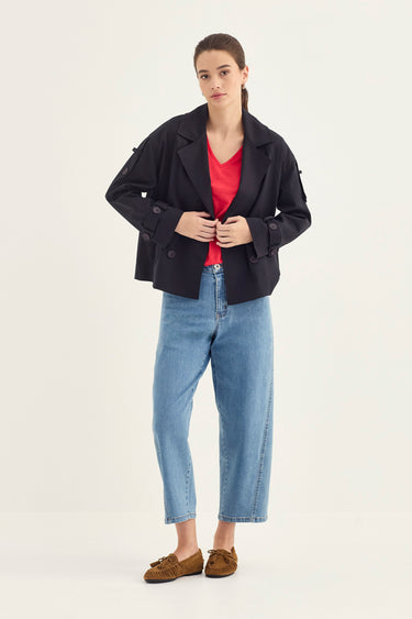 A woman modeling a dark navy blue blazer over a red V-neck top, paired with light blue cropped jeans by Verge and brown suede loafers, against a plain off-white studio background