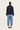 A model viewed from the back wearing a dark navy cropped jacket with sleeve tabs and light blue cropped jeans by Verge, paired with brown slip-on shoes, against a plain off-white studio background.