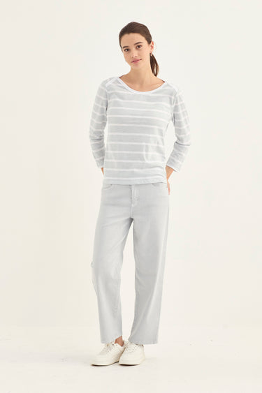 A woman modeling a light gray and white striped long-sleeve top with matching light gray wide-leg pants and white sneakers by Verge, standing against a plain white studio background.