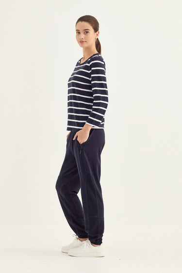 A woman modeling a navy blue and white horizontally striped long-sleeve top paired with dark navy jogger pants and white sneakers by Verge, standing against a plain white studio background.