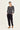 A woman modeling a black and white horizontally striped long-sleeve top with black jogger pants by Verge and brown shoes, standing against a plain white studio background.