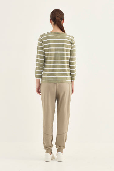 A woman viewed from the back wearing a long-sleeve top with horizontal olive green and white stripes, paired with beige jogger pants by Verge and white sneakers, against a plain light background.
