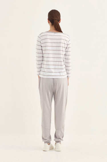 A woman viewed from behind wearing a white long-sleeve top with thin gray horizontal stripes and light gray jogger pants by Verge, standing against a plain off-white studio background.