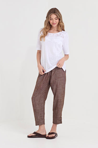 A woman modeling a white short-sleeve top and brown textured cropped pants by Verge with dark brown sandals, standing against a plain light background.