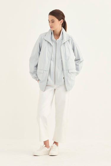 A woman modeling a light gray lightweight jacket over a white top and white wide-leg cropped pants by Verge, paired with white sneakers, against a plain white studio background.