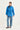 A woman modeling a bright blue lightweight jacket with a high collar, front zipper, and drawstring waist, paired with light blue jeans by Verge and dark flats, against a plain light gray studio background.