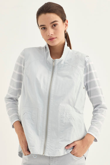 A woman wearing a light gray zip-up vest over a white striped long-sleeve shirt by Verge, photographed against a plain light background.