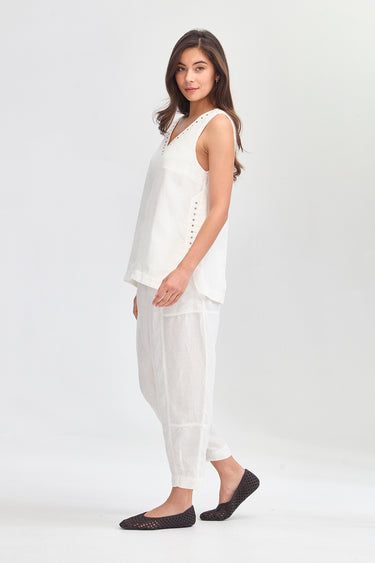 A woman modeling a white sleeveless top and matching loose white pants by Verge, paired with black flats, against a clean white studio background.