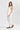 A woman modeling a white sleeveless tank and matching loose white pants by Verge, paired with black flats, against a clean white studio background.