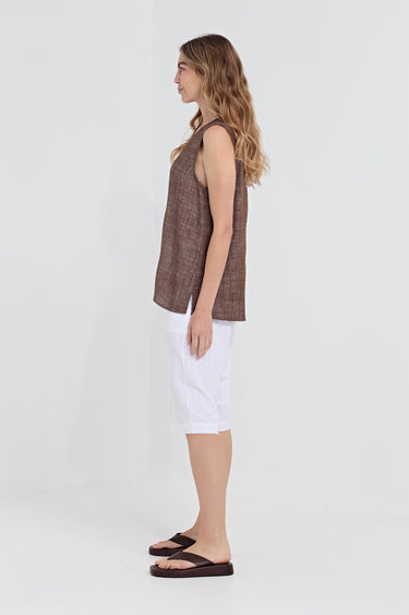 A woman shown in profile wearing a sleeveless brown textured top, white shorts by Verge, and dark brown sandals against a plain light gray studio background.