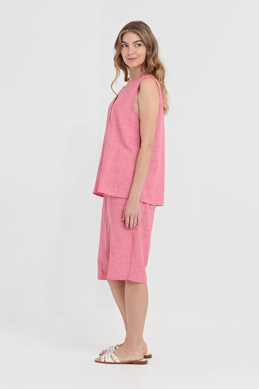 A woman modeling a pink sleeveless linen vest and matching midi-length linen shorts by Verge against a plain white studio background.