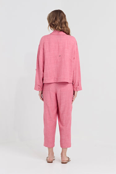 A woman viewed from the back wearing a pink two-piece linen set consisting of a cropped jacket and cropped trousers by Verge, paired with flat sandals, against a plain white studio background.