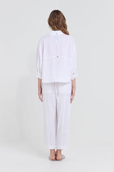 A woman viewed from the back wearing a white linen two-piece set consisting of a jacket and matching wide-leg trousers by Verge, set against a plain light gray studio background.