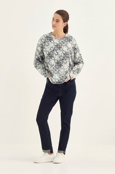 A woman modeling a long-sleeve crewneck sweatshirt with a black and white abstract pattern by Verge, paired with dark navy pants and white sneakers, against a plain white studio background.