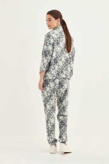 A woman modeling a matching two-piece snake print set by Verge, shown from the back against a plain white studio background.