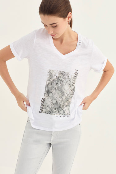 A woman wearing a white short-sleeve V-neck t-shirt with a black and gray snakeskin print panel on the front, paired with light gray jeans by Verge, against a plain off-white background.