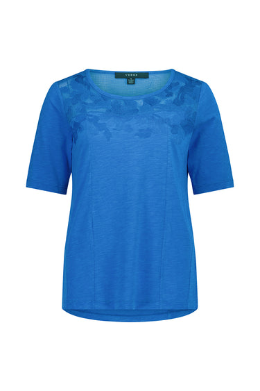 A sapphire blue short-sleeve top by Verge with a sheer floral lace overlay across the chest, displayed on a clean white background.