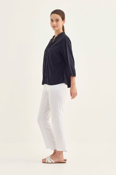 A woman modeling a dark navy blue long-sleeve blouse and white cropped trousers by Verge, standing against a plain white studio background.
