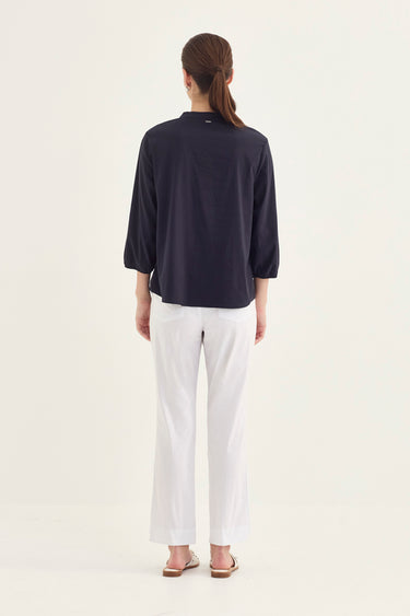 A woman viewed from the back wearing a dark navy three-quarter sleeve top and white cropped pants by Verge, standing against a plain light background.