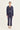 A model stands against a plain light background wearing a matching navy blue cropped jacket and cropped pants set by Verge, with a white top peeking out at the collar and white sandals.