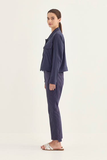 A woman stands in profile wearing a matching navy blue lounge set consisting of a cropped long-sleeve top and straight-leg pants by Verge, paired with white slide sandals, against a plain off-white studio background.
