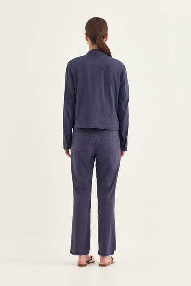 A woman viewed from the back wearing a matching navy blue two-piece set consisting of a cropped long-sleeve jacket and wide-leg trousers by Verge, set against a plain off-white studio background.