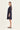 A woman modeling a dark navy blue shift dress by Verge with three-quarter sleeves, shown in profile against a plain off-white studio background.