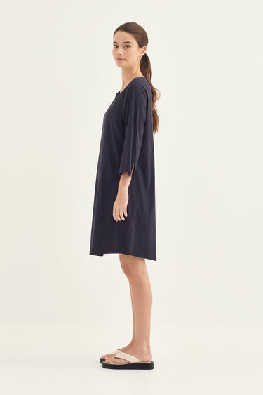 A woman modeling a dark navy blue shift dress by Verge with three-quarter sleeves, shown in profile against a plain off-white studio background.
