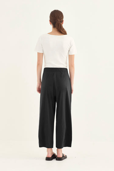 A woman viewed from behind wearing a white short-sleeve top and black wide-leg cropped pants by Verge, standing against a plain light background.