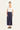 A woman modeling a white short-sleeve scoop-neck top and navy blue wide-leg cropped pants by Verge, paired with black sandals, against a plain white studio background.