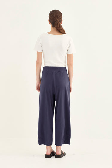 A woman viewed from the back wearing a white short-sleeve top and navy wide-leg cropped pants by Verge, standing against a plain white studio background.