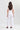 A woman viewed from behind wearing a white short-sleeve top and white wide-leg cropped pants by Verge, standing against a plain light gray studio background.