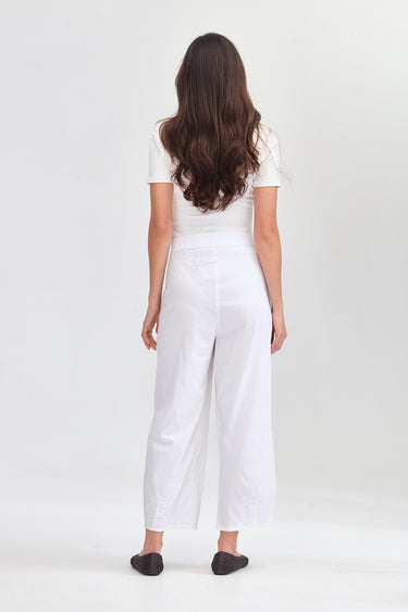 A woman viewed from behind wearing a white short-sleeve top and white wide-leg cropped pants by Verge, standing against a plain light gray studio background.