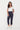 A woman modeling a white short-sleeve top and navy blue cropped pants by Verge with white sneakers, standing against a plain white studio background.