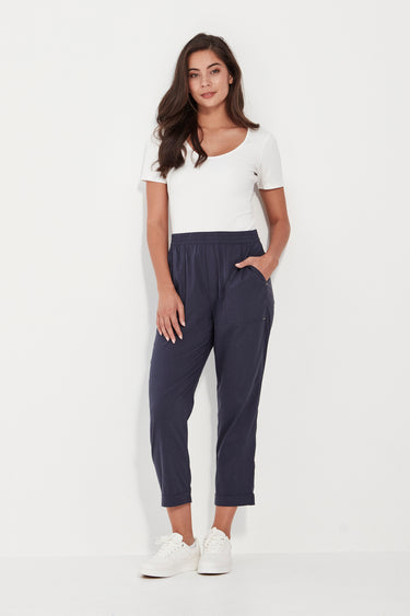 A woman modeling a white short-sleeve top and navy blue cropped pants by Verge with white sneakers, standing against a plain white studio background.