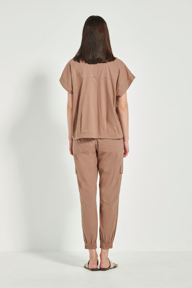 A woman viewed from the back wearing a matching taupe-brown short-sleeve top and cargo-style pants set by Verge, standing against a plain light gray studio background.