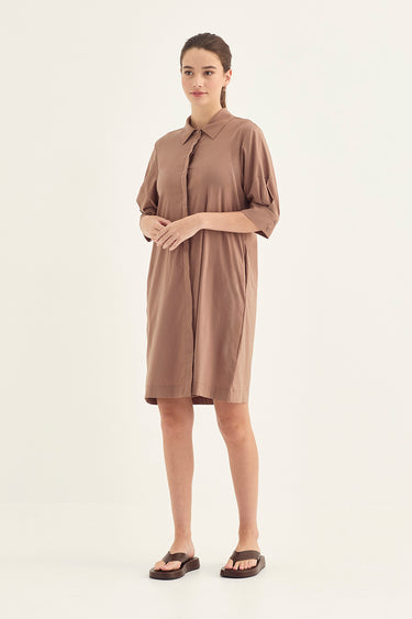 A woman modeling a short-sleeve, collared brown dress by Verge with a button placket, photographed against a plain light background.