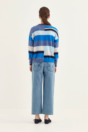 Person wearing a blue and white striped sweater and light blue jeans by Verge on a white background