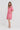 A woman modeling a pink linen-blend tunic dress by Verge with short sleeves, a drawstring neckline, and side pockets, standing against a light gray studio background.
