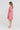 A woman wearing a pink short-sleeve linen dress by Verge with a relaxed, oversized fit and side slits, standing in profile against a clean white studio background.
