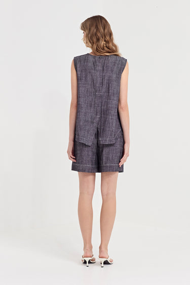 A woman viewed from the back wearing a sleeveless tank, in ink colour with matching shorts by Verge, paired with white heeled sandals, against a plain white studio background.