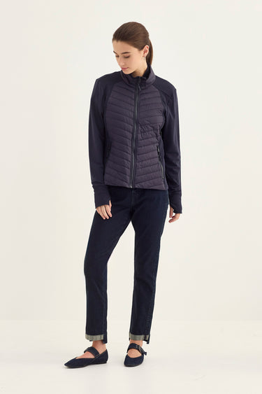 A woman modeling a dark navy blue quilted zip-up jacket with matching dark navy pants by Verge and flats, standing against a plain off-white studio background.