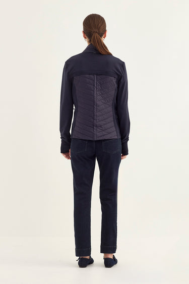 A woman viewed from the back wearing a dark navy quilted jacket with long sleeves and matching dark navy pants by Verge, standing against a plain light background.