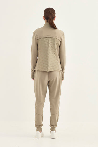 A model viewed from the back wearing a light beige matching set consisting of a long-sleeve cropped quilted jacket and matching jogger pants by Verge, paired with white sneakers against a plain white studio background.