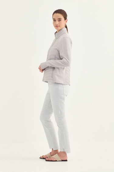 A woman modeling a light gray zip-up jacket and matching light gray pants by Verge, against a plain white studio background.