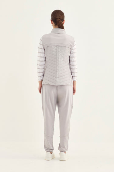 A model viewed from the back wearing a light gray two-piece outfit consisting of a quilted puffer vest over a striped long-sleeve top and matching gray jogger pants by Verge, on a plain white studio background.