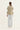 A model shown from the back wearing a beige quilted vest over a white and beige striped long-sleeve shirt, paired with light gray trousers and white sneakers by Verge, against a plain white studio background.